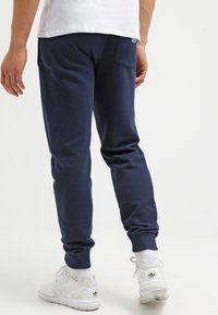 Marinblå joggerbyxor tillverkade av mjuk bomull, med elastiska cuffs, sidofickor och en bakficka med etikett-detalj.