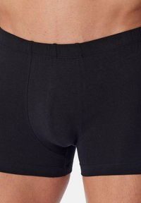 Närbild av en person som bär svarta åtsittande boxerkalsonger, som visar midjebandet och övre låren.
