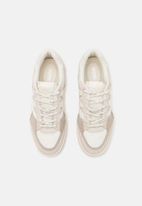 Sneaker bianco e beige con pannelli testurizzati, punta rotonda, lacci piatti e colletto imbottito con marchio sulla soletta.