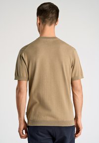 Καφέ πλεκτό t-shirt με κοντά μανίκια, λαιμόκοψη σε στρογγυλό σχήμα και λεπτομέρειες με υφή στο ράψιμο. Ομαλό ύφασμα με εφαρμοστή σιλουέτα.