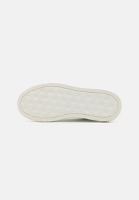 Fehér sneaker talp, texturált, kockás mintázattal. Lekerekített szélek és bordázott díszítés a perem mentén. Tiszta, minimalista dizájn.