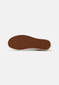 Semelle de chaussure avec un motif de bande de roulement en caoutchouc brun en forme de gaufre et un bord blanc, vue de dessous sur un fond blanc.