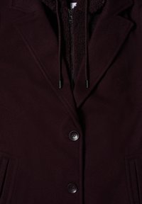 Bordeaux wolmengsel jas met een gewatteerde fleece interieur, twee knopen en zijzakken. Ritssluiting aan de voorkant met trekkoordaccenten.