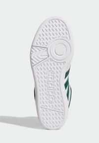 Biała gumowa podeszwa buta z teksturowanym wzorem antypoślizgowym, wytłoczonym logo oraz zielonymi akcentami bocznymi z trzema białymi paskami.