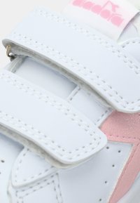 White sneaker with pink accents; features two Velcro straps, a smooth surface, and contrasting white stitching. Notable brand logo on the tongue.