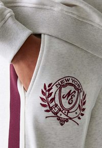 Helle graue Sweatshirt mit einem bordeauxroten gestickten Emblem mit "NEW YORK" und einem Lorbeerdesign, gerippten Bündchen und seitlichen Taschendetails.