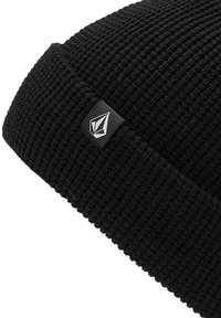 Cappello in maglia nera realizzato in tessuto testurizzato, con una piccola etichetta logo nera e bianca sul lato.