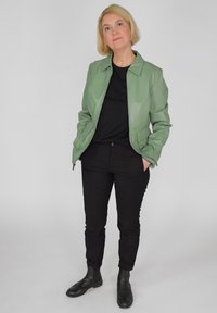Groene leren jas met een rechte snit en ritsmanchetten; gecombineerd met een zwarte top en slanke zwarte broek; gedragen met zwarte enkellaarsjes.