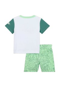 T-shirt bianca con maniche corte verdi, abbinata a pantaloni corti verdi con un motivo grafico giocoso e accenti del logo "Nike".