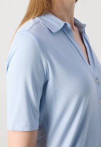 Polo shirt azzurro chiaro a maniche corte con colletto, dotato di patta con bottoni e una texture liscia e morbida. Brillantezza sottile e design aderente.