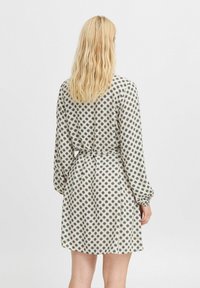 Rochie cu mâneci lungi, dintr-un material ușor, de culoare crem, cu un model circular negru, cintrată în talie, având un rând de butoane la spate.