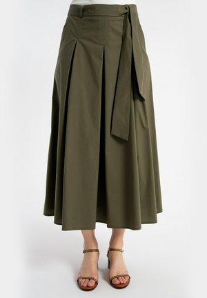 Miodowa zielona spódnica midi kopertowa z przednimi zakładkami i wiązanym paskiem, noszona z brązowymi sandałami na obcasie z odkrytymi palcami i paskiem wokół kostki.