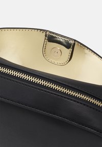 Interno di una borsa a tracolla nera in pelle con una fodera dorata riflettente. Presenta una cerniera dorata e un dettaglio di chiusura a scatto.