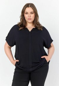 Top nero a maniche corte con scollatura a V, realizzato in un materiale morbido. Presenta una vestibilità rilassata ed è abbinato a pantaloni scuri.