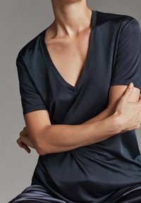 Dark navy v-neck t-shirt with short sleeves, smooth texture, and a relaxed fit, worn with arms crossed against a neutral background.