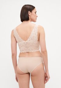Lace bralette in nude with intricate floral patterns and wide lace straps. Matched with seamless nude panties featuring scalloped edges.