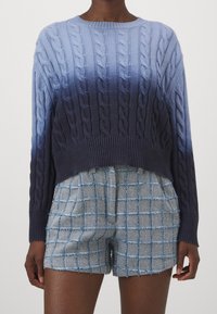 Stickad tröja i gradientblått med ett kabelmönster och ribbad fåll. Matchas med ljusblå rutiga shorts, tillverkade av texturerat tyg.