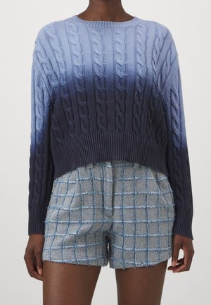 Pull en tricot dégradé bleu, avec un motif en torsades et un ourlet côtelé. Associé à un short à carreaux bleu clair, fabriqué dans un tissu texturé.