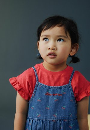 Sukienka dżinsowa z wzorem wiśni na czerwonej koszuli z falbanami. Posiada regulowane ramiączka i marszczoną talię. Codzienny strój dziecka.