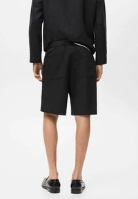 Shorts en lin noir à coupe droite, avec deux poches arrière, associés à un haut noir à manches longues. Texture lisse et design minimaliste.