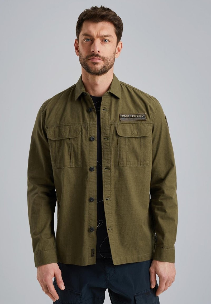 Camicia button-up verde oliva con due tasche sul petto, una patch tessuta etichettata "PME Legend" e maniche lunghe. Il tessuto ha una finitura testurizzata.