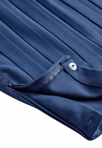 Tessuto blu navy con pieghe verticali, dotato di chiusura con zip e bottone a scatto argentato. Texture liscia e materiale resistente.