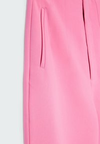 Gros plan sur un pantalon rose taillé sur mesure avec une poche latérale fendue et une texture de tissu lisse.