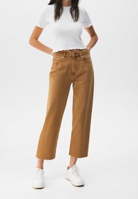 Jeans marron à jambes larges et taille haute, associés à un haut court côtelé blanc. Coupe droite avec coutures simples. Complétés par des baskets blanches.