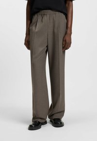 Brown, textured wide-leg trousers with an elastic waistband. Features a subtle pattern and a smooth finish, paired with black shoes.