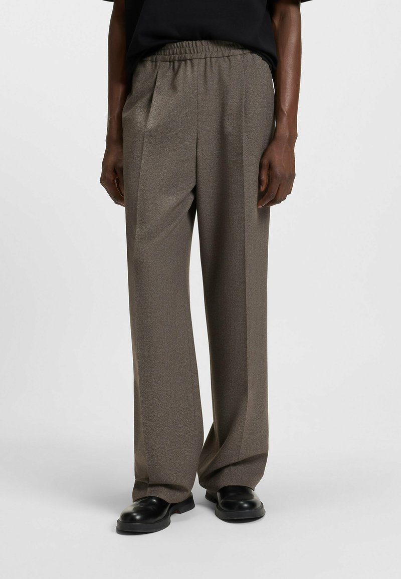Brown, textured wide-leg trousers with an elastic waistband. Features a subtle pattern and a smooth finish, paired with black shoes.