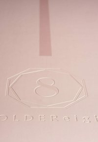 Lichtroze textiel met een gestructureerd oppervlak, met een reliëf octogonale logo waarin het cijfer "8" in het midden staat en "GOLDEReight" eronder.