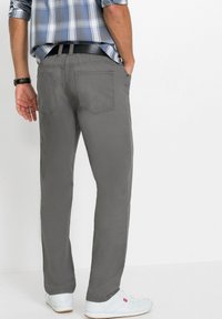 Pantaloni di cotone grigi con tasche posteriori, design a gamba dritta e una texture liscia. Abbinati a sneakers bianche e una camicia a quadri blu.