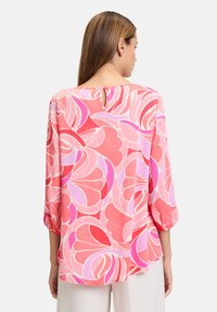 Blusa fluida in fantasia floreale rosa e rossa, con maniche a tre quarti e dettaglio a chiave sul retro, realizzata in tessuto leggero.