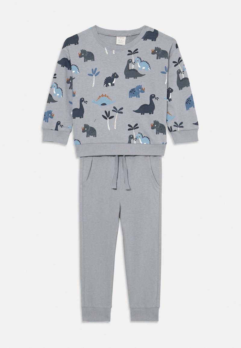 Grijze kindertrainingsoutfit met een lange mouwen top met dino-afdrukken in blauw en zwart, gecombineerd met bijpassende joggerbroeken met trekkoord.