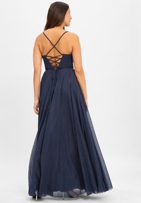 Marineblaue bodenlange Kleid mit tailliertem Oberteil, Spaghettiträgern und Kreuzdetails im Rücken. Hergestellt aus einem glitzernden, fließenden Stoff.