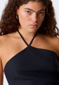 Musta halterneck-mekko, jossa on pinstripe-kuvio, tyylikäs kangas ja ohuet hihnat. Suunniteltu istuvaksi ja sileäksi.