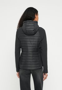 Μαύρο μπουφάν μ�ε επένδυση και εφαρμοστό κουκούλα, με υφή καπιτονέ στην πλάτη, λεία μανίκια και ελαστικές μανσέτες. Σχεδιασμένο για ζεστασιά και άνεση.