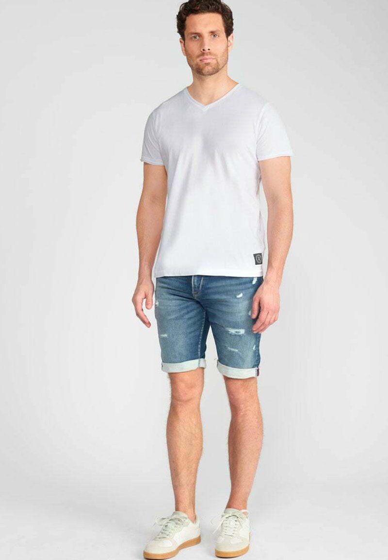 Witte katoenen V-hals t-shirt, blauwe denim shorts met opgerolde mouwen, en witte sneakers met een lichtbruine zool. Beschadigde details op de shorts.