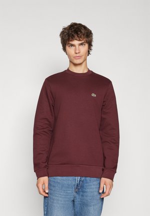 Maroon sweatshirt with long sleeves and a crew neckline, featuring a small green logo on the chest. Made from a soft, textured fabric.