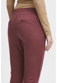 Burgundy joggers i stretchy tyg, med elastisk midja, två bakfickor och en slät yta.