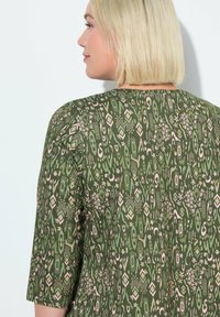 Groene stof met een geometrisch patroon in tinten van roze en crème; heeft een ronde halslijn en driekwart mouwen.