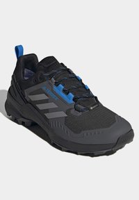 Czarne buty sportowe z niebieskimi akcentami, teksturowana siateczka na wierzchu, gumowa podeszwa i trzy szare paski po boku. Posiadają wzmocnioną noskę.