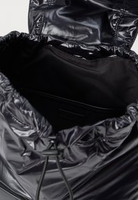 Μαύρο, γυαλιστερό εσωτερικό τσάντας με απαλή υφή, με κορδόνι στο επάνω μέρος και ξεχωριστή εσωτερική τσέπη. Διακριτική επωνυμία είναι ορατή.