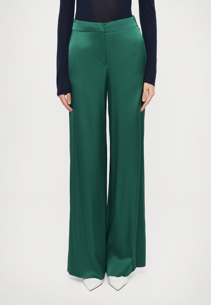 Laiade rohelised satiinsed püksid, millel on sile tekstuur, kõrge vöökoht ja varjatud esikitsel. Kombineeritud valgete teravate ninakulega kingadega.