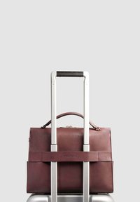 Bordeauxrote Lederaktentasche mit einem oberen Griff, präsentiert auf einem Koffer. Verfügt über eine glatte Textur, Metallbeschläge und ein Logo auf der Vorderseite.