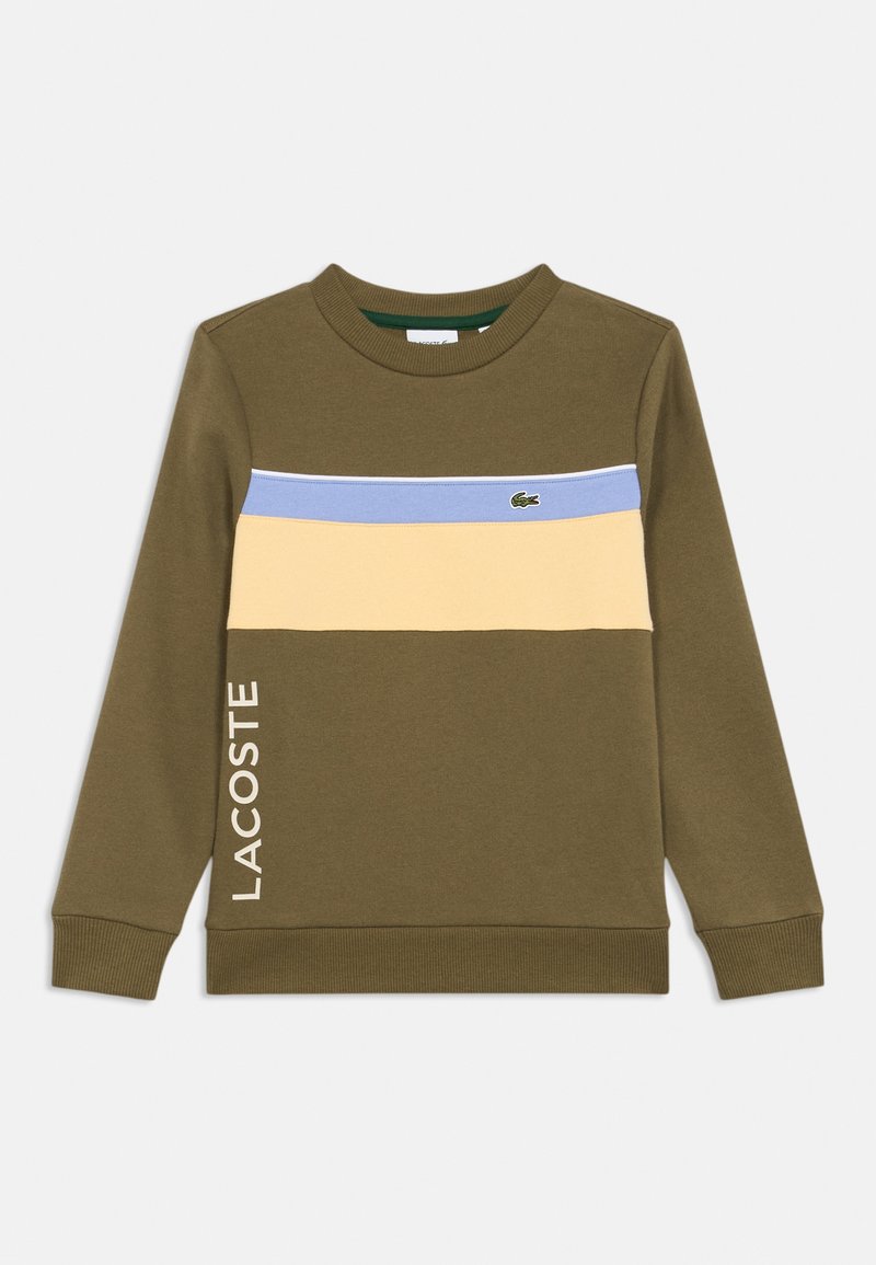 Ελαιοπράσινη μπλούζα με ρεγκλάν λαιμό, με οριζόντιες ρίγες σε ανοιχτό μπλε, κίτρινο και λευκή ρίγα. Το "LACOSTE" εκτυπωμένο κάθετα.