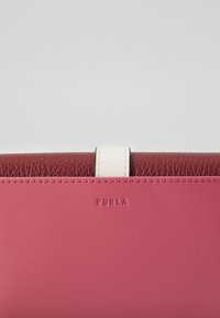 Furla piniginė su dviejų tonų dizainu; tekstūruoto bordo viršus ir glotnus rožinis dugnas. Yra balta akcentinė juostelė ir iškilminis logotipas.