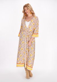 Rochie kimono floral în galben și portocaliu, având o siluetă înfășurată, mâneci trei sferturi și o talie legată. Detaliată cu accente decorative.