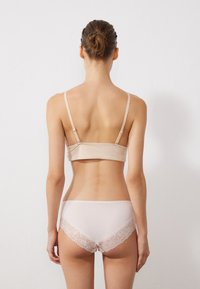Bralette beige con spalline sottili abbinato a mutandine rosa chiaro con bordi in pizzo. Tessuto liscio con un design aderente.