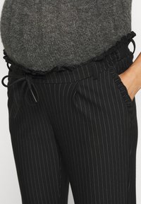 Pantalones a rayas negros con cintura voluminosa, cierre de cordón y bolsillos laterales; hechos de una tela suave y texturizada.